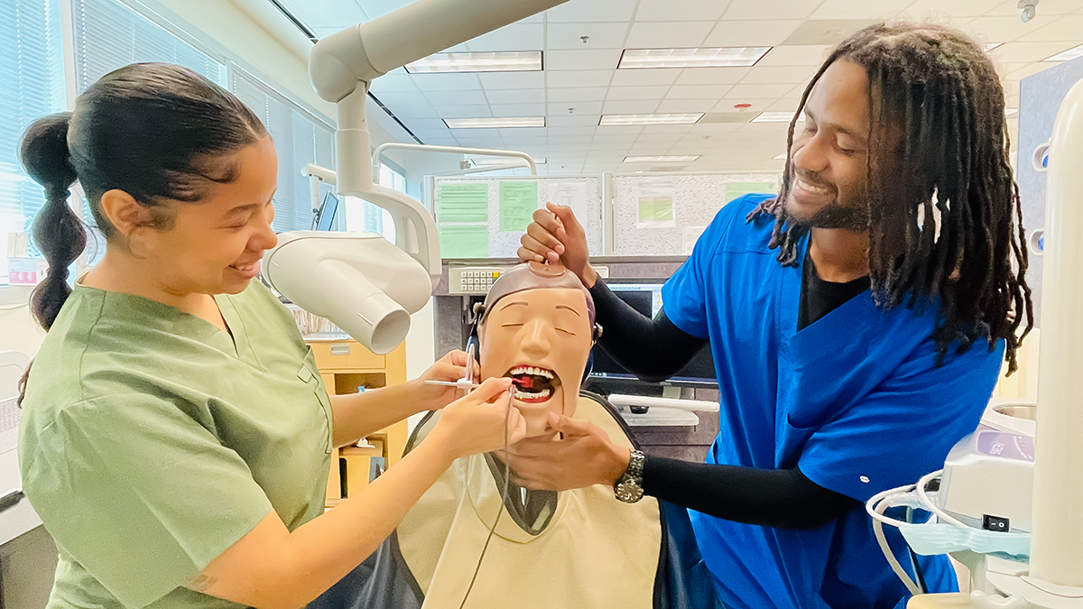 Dental Hygienist demonstrating to a student how to perform a cleaning on a mannequin.